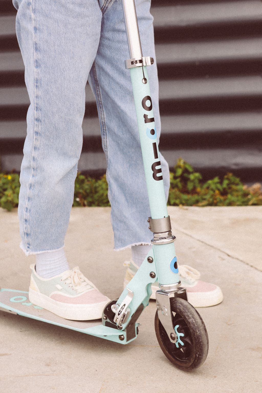 Barn kører på Micro løbehjul, iført lyseblå jeans og lyse sneakers.