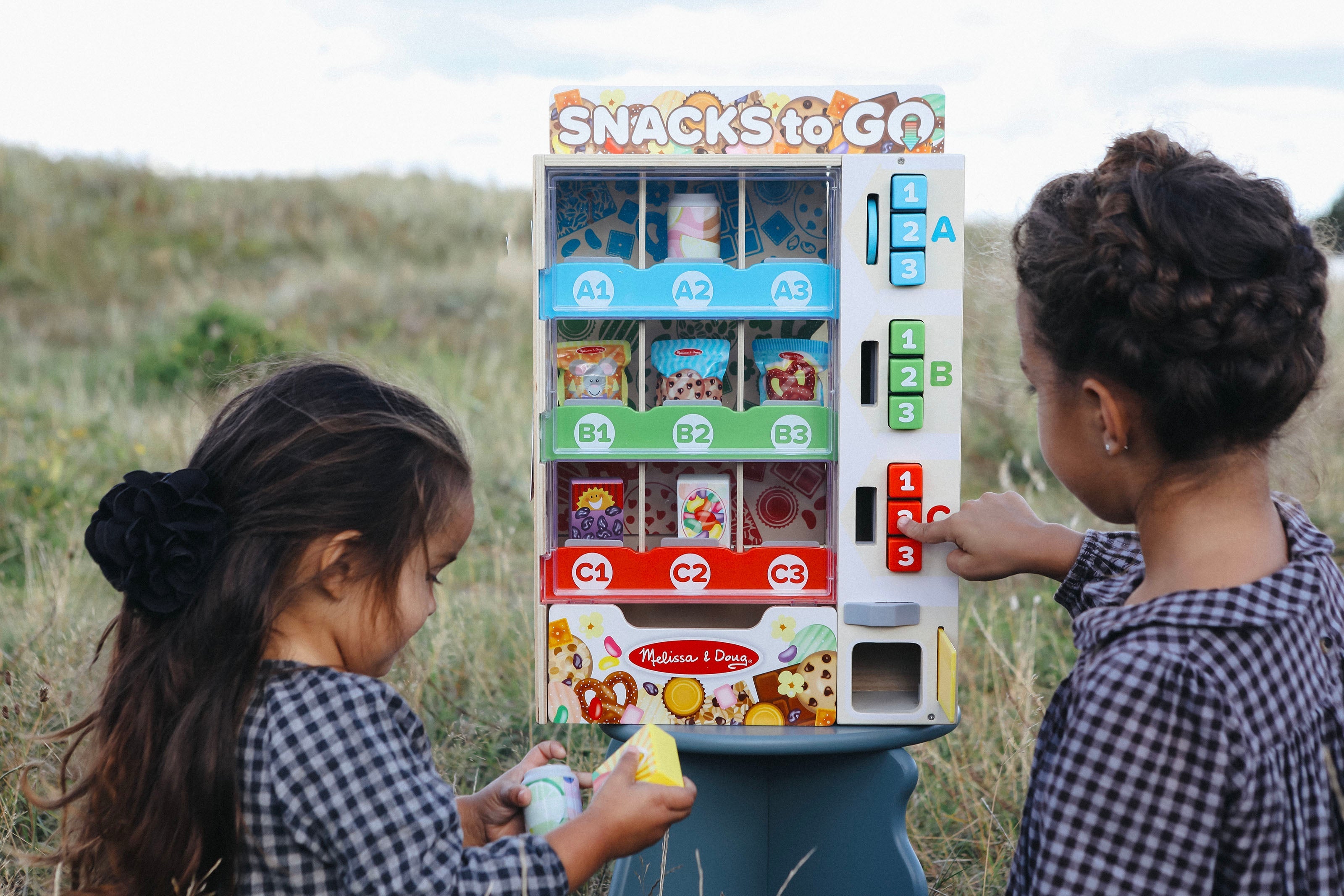 To piger leger med en snackautomat fra Melissa & Doug udendørs