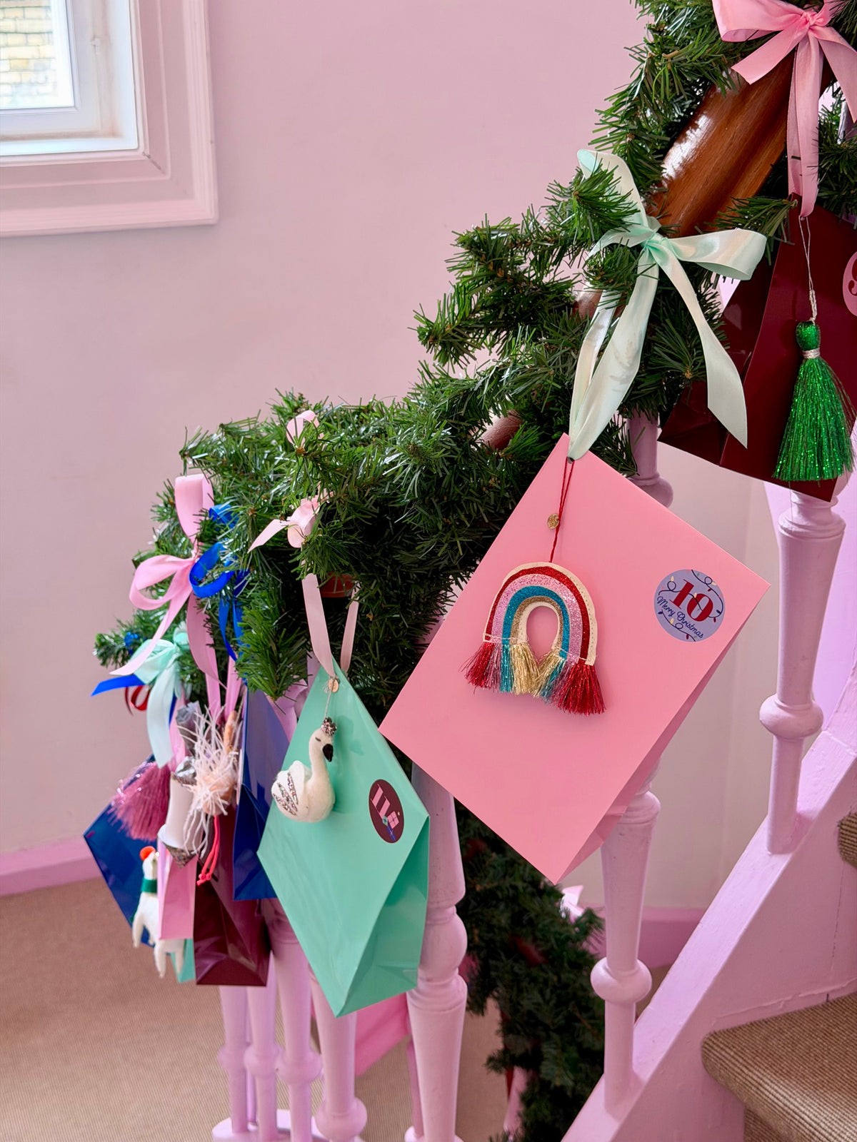 Pakkekalender gaver hængende på pink trappegelænder med granguirlande
