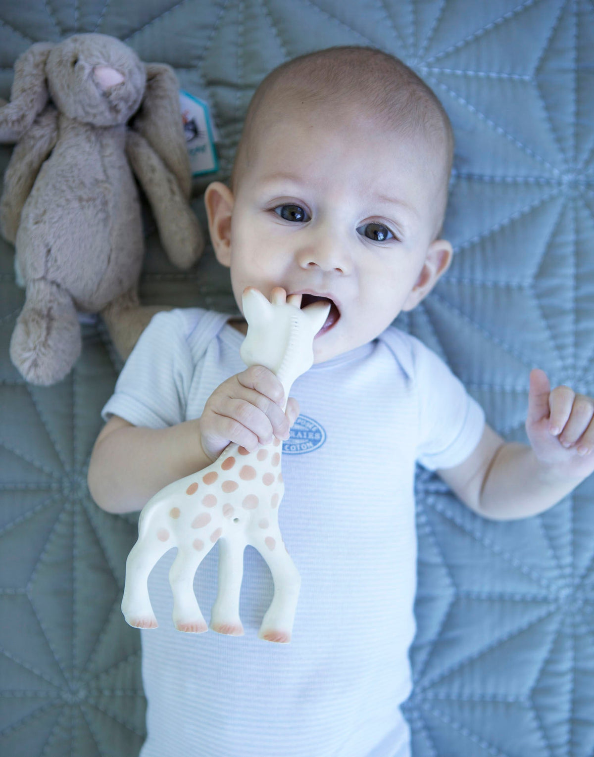 Baby med Sophie la girafe bidering og bamse på et tæppe.