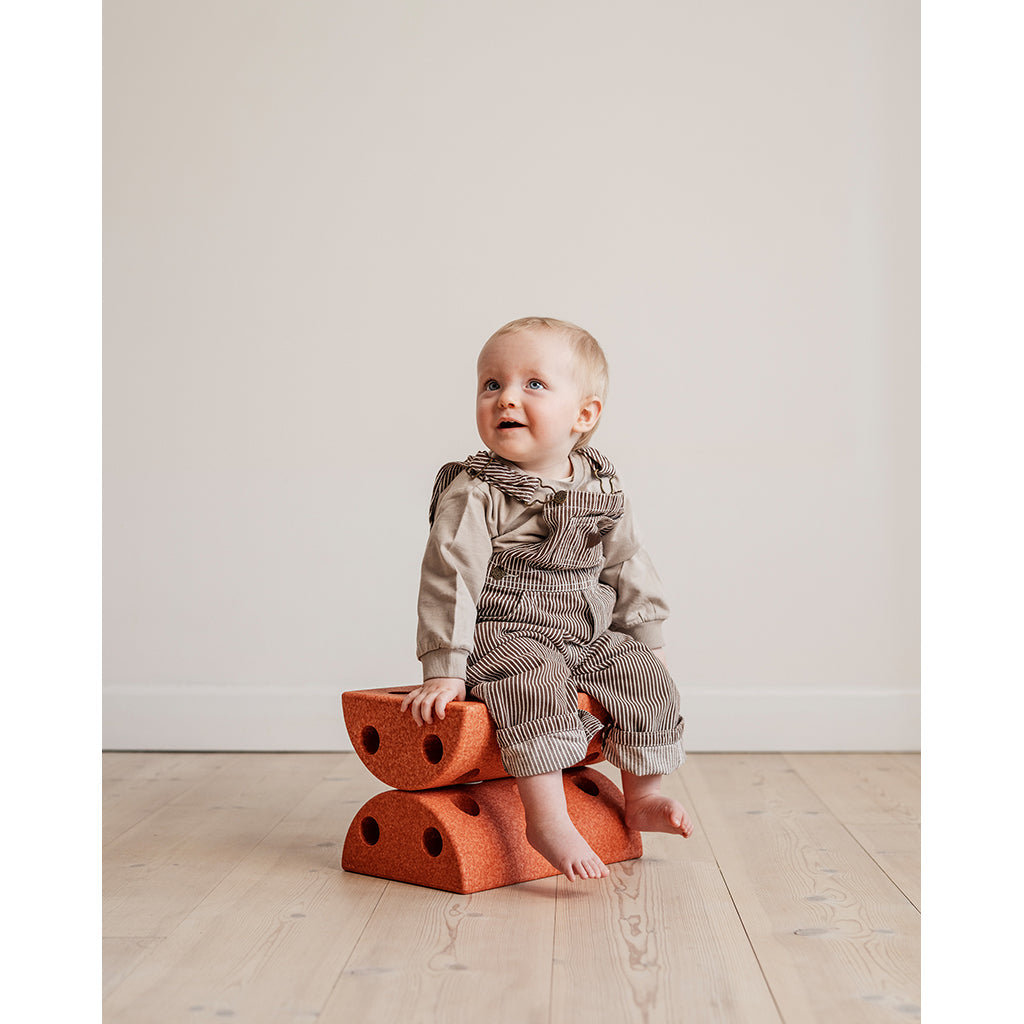 Baby sidder på to brændt orange Modu skamler på trægulv.