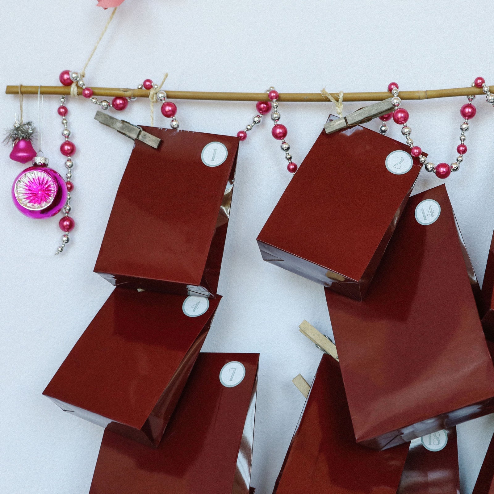 Pakkekalender med røde gaveposer, pink perler og julepynt