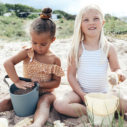 To små piger leger med strandsand og spande på stranden