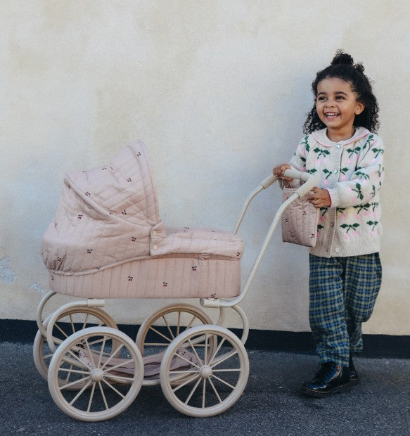 Smilende pige skubber Konges Sløjd Minnie dukkevogn i cherry blush design med taske