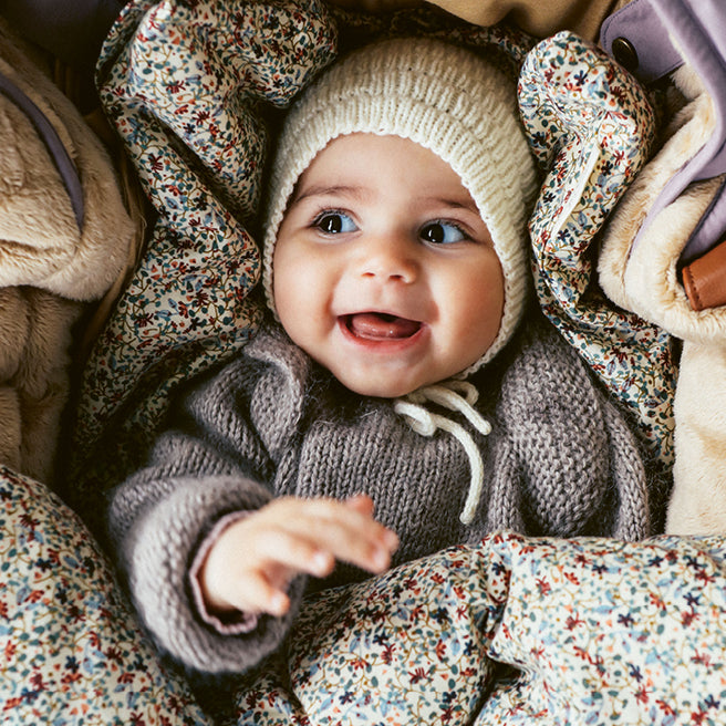 Glæd baby i strikket huesæt i den hyggelige babynest