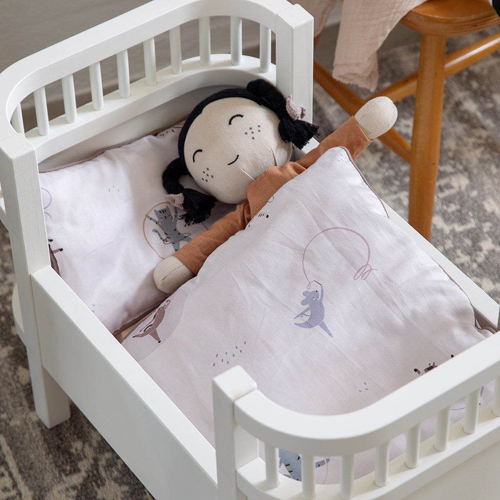 Sebra stofdukke med flettet sort hår sover i hvid dukkeseng med dyne og pude