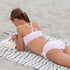 Pige i lyserød Petit Crabe UV bikini ligger på strand og læser bog